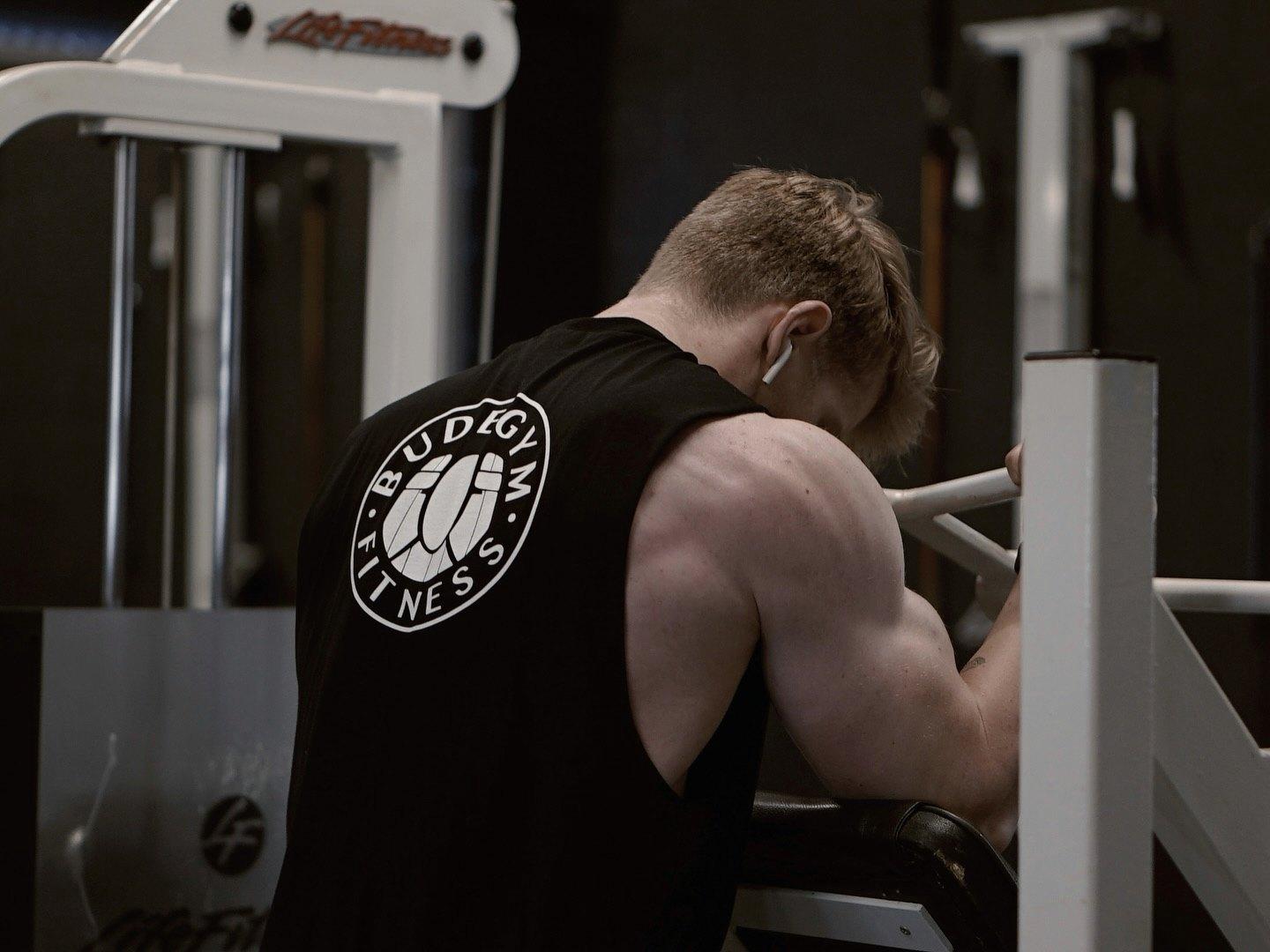 A member in a Bude Gym vest on a machine, seen from behind